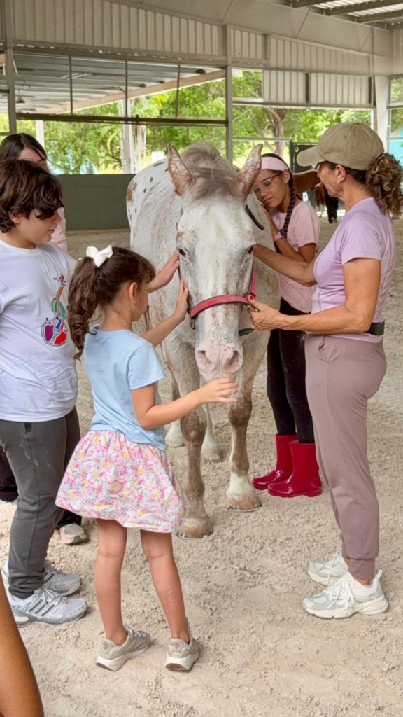 Niños acariciando un caballo junto con una de las terapeutas
